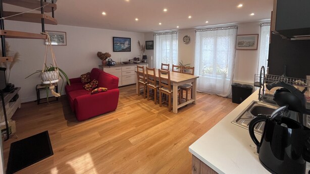 A modern kitchen with wooden cabinets, a dining area with a red sofa, and a staircase. - House two minutes from the beach (barfleur)