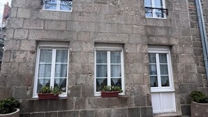A stone building with three windows, each with a white frame and a small balcony. There are potted plants on the windowsills. - House two minutes from the beach (barfleur)