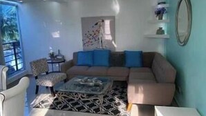 Ein modernes Wohnzimmer mit Sofa, Couchtisch, einem gemusterten Teppich, einem Sessel, einem kleinen Tisch und einem Deckenventilator.