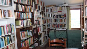 Een kamer met een houten tafel, een groene fauteuil en meerdere boekenplanken vol boeken.