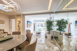 Ein moderner Essbereich mit Glastisch, Stühlen und einer Chandelier. Es gibt Blumentöpfe und Kunstwerke an den Wänden.