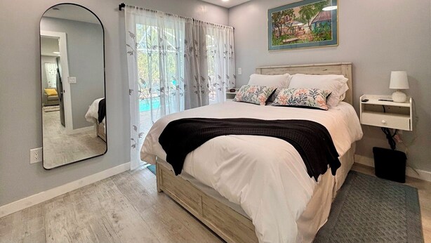 Een slaapkamer met een bed, nachtkastje, lamp, spiegel en een schilderij aan de muur.