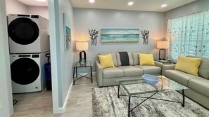 A living room with a sofa, a glass coffee table, and a wall-mounted painting. - Mangrove Nest (Fort Myers Beach)
