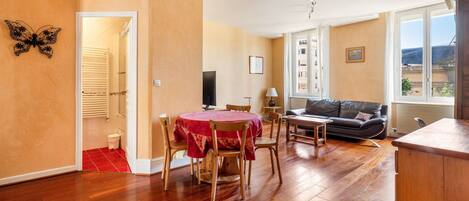 A room with a dining table, chairs, a sofa, a TV, and a window with a view.