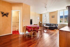 A room with a dining table, chairs, a sofa, a TV, and a window with a view. - Lyon 6 Foch: Quiet 1-bedroom apartment with workspace (Lyon)
