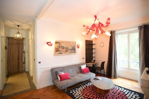 Ein Wohnzimmer mit einer Couch, einem Couchtisch, einem Gemälde an der Wand, einer Kandelaber und einem Fenster mit Vorhängen.