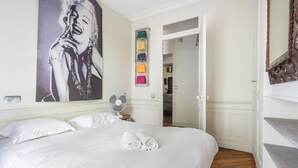 Ein Hotelzimmer mit einem großen Bett, einem Wandventilator, einem Gemälde und Blick zur Küche.