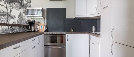 Cocina compacta con alacenas blancas, microondas integrado, cafetera y estufa.