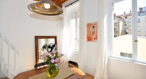 A dining area with a wooden table, a vase with flowers, a mirror, and a window with a view of buildings. - Apartment 'Sainte Clotilde' with Wi-Fi (Lyon)