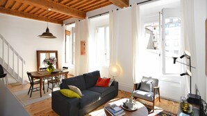 Sala de estar com sofá, mesa de jantar com cadeiras, luminária e vista para o exterior.