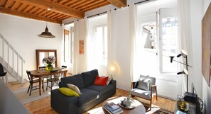 A living room with a sofa, a dining table with chairs, a lamp, and a view of the outside. - Apartment 'Sainte Clotilde' with Wi-Fi (Lyon)