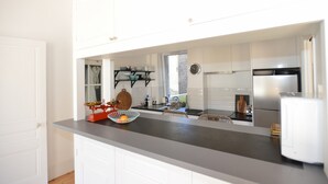 Cozinha moderna com armários brancos, bancada cinzenta, uma balança vermelha e uma tigela com laranja.