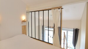 Un dormitori amb un llit, una petita taula de nit amb una làmpada, una finestra amb cortines i vista a l'exterior.