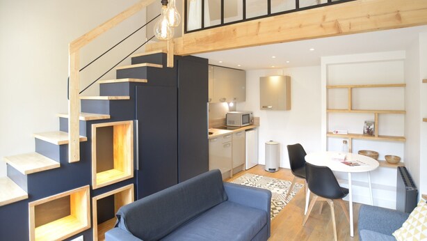 Un apartament modern amb una escala, una zona d'estar amb sofà, taula de dinar amb cadires i prestatges de disseny.