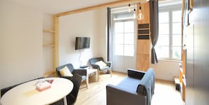 Een moderne woonkamer met een flatscreen televisie, twee banken, een kleine tafel en een raam met gordijnen.