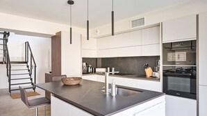 Una cocina moderna con una isla central, electrodomésticos integrados y una escalera que sube a otro nivel.
