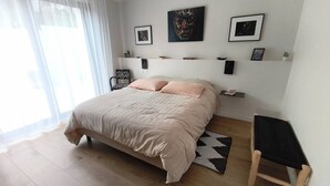 Un dormitorio con cama, una silla, un tapete y estantes en la pared con cuadros.