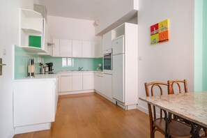 A modern kitchen with white cabinets, a dining table, and a colorful wall clock. - Lyon 2 presqu'ile: 2-bdr spacious apartment (Lyon)