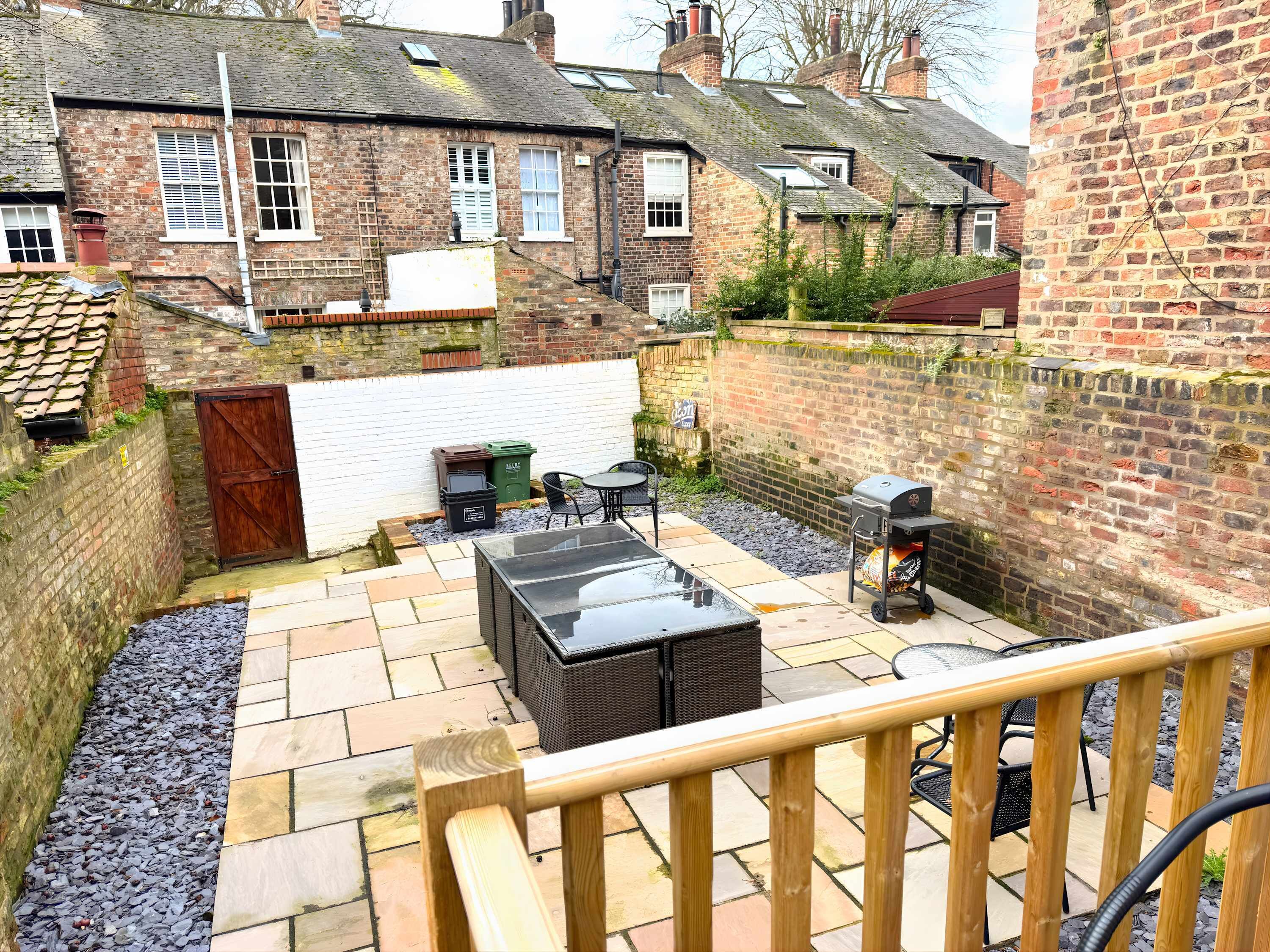 A courtyard with a barbecue grill, outdoor seating, and a wooden staircase.