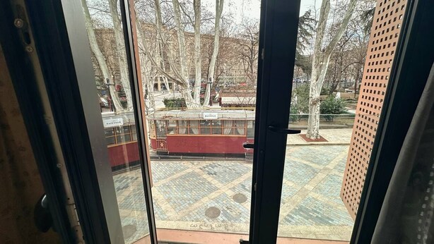 Vista a través de una ventana con suelo de baldosas, un edificio rojo y árboles.