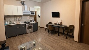 Una cocina compacta con lavadora, una mesa de comedor con sillas y un televisor montado en la pared.