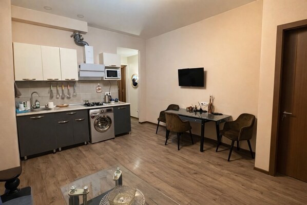 A compact kitchen with a washing machine, a dining table with chairs, and a TV mounted on the wall. - Central Orbeliani Palazzo (Tbilisi)