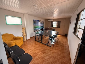 Una habitació amb una taula de vidre, cadires, un sofà groc, una estàtua i un quadre a la paret.