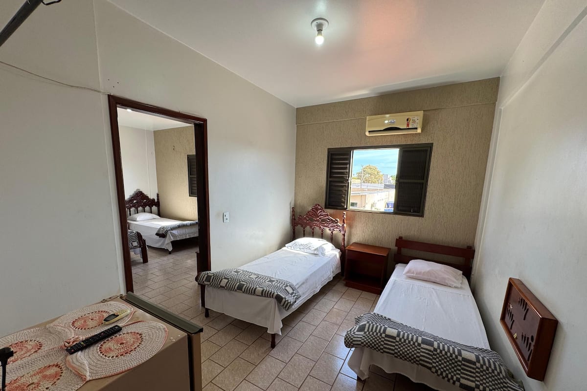 Una habitación con dos camas individuales, una mesita con un control remoto, un espejo y un equipo de aire acondicionado.