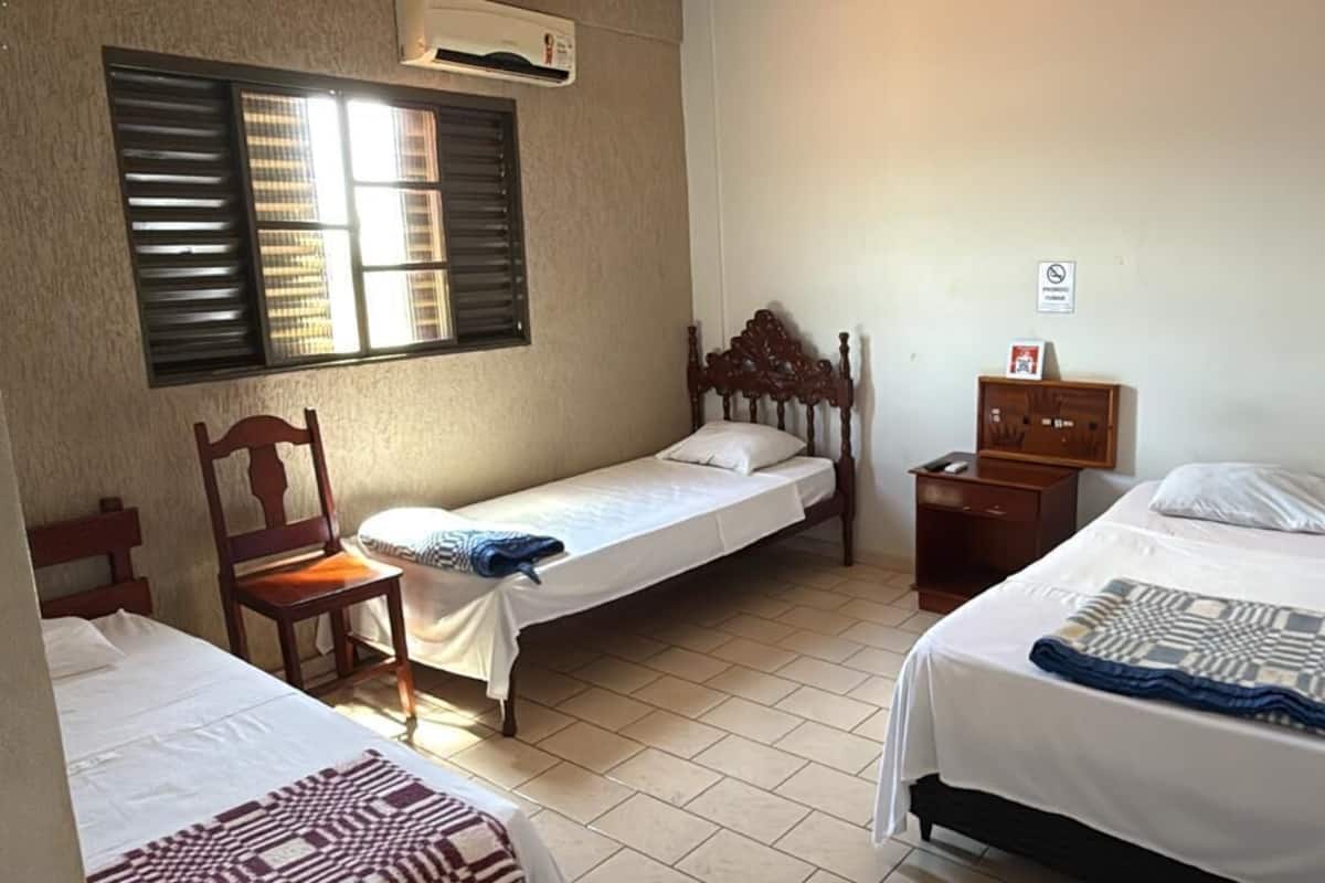 Una habitación con dos camas, una silla, una mesita de noche y una ventana con contraventanas.