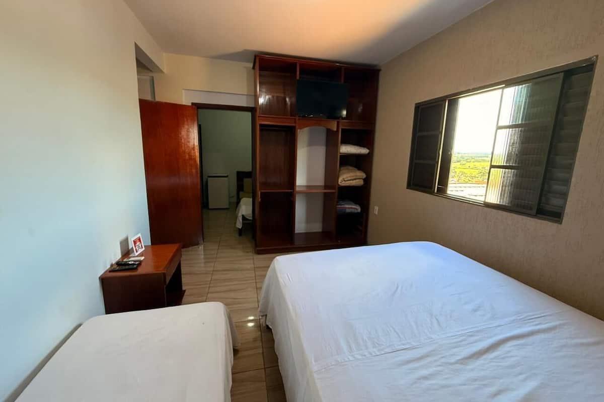 Habitación de hotel con dos camas, un armario de madera, una televisión y una ventana con vistas.