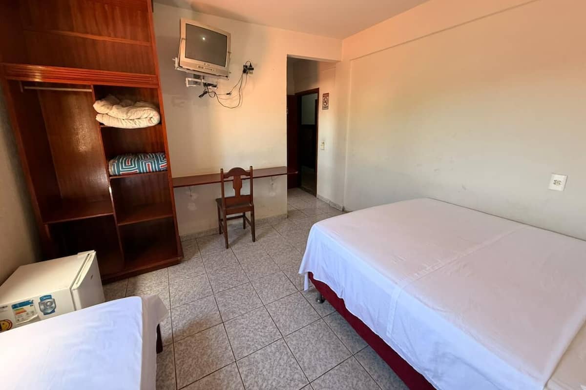 Una habitación con cama, un armario de madera, una silla, un escritorio y un televisor montado en la pared.