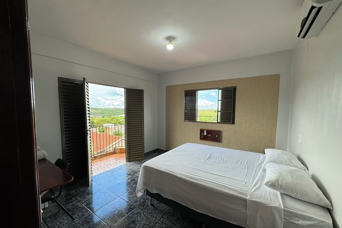 Un dormitorio con cama, escritorio, ventana con vistas y aire acondicionado.