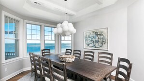 Un comedor con una mesa grande, seis sillas, un candelabro y vista al océano.