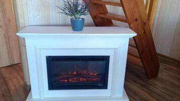 Une cheminée blanche sur laquelle est posé un pot bleu, une échelle en bois appuyée contre, et un feu qui brûle à l’intérieur.