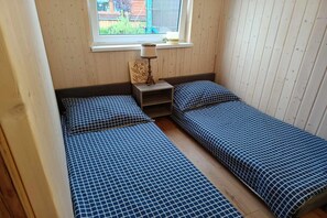 A small room with two single beds, a nightstand, a lamp, and a window.