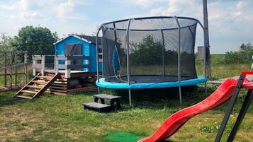 Ein Trampolin mit Sicherheitsnetz, eine Rutsche, ein kleines blaues Spielhaus und eine Holztreppe, die zum Spielhaus führt.