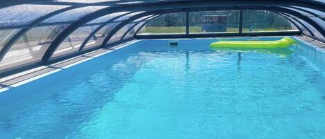 Una piscina interior con agua azul cristalina, un flotador hinchable verde y vistas al exterior a través de un techo de vidrio.