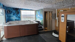 Une pièce dotée d’un grand jacuzzi, d’une fresque représentant un paysage tropical, d’un sauna et offrant une vue par une fenêtre.