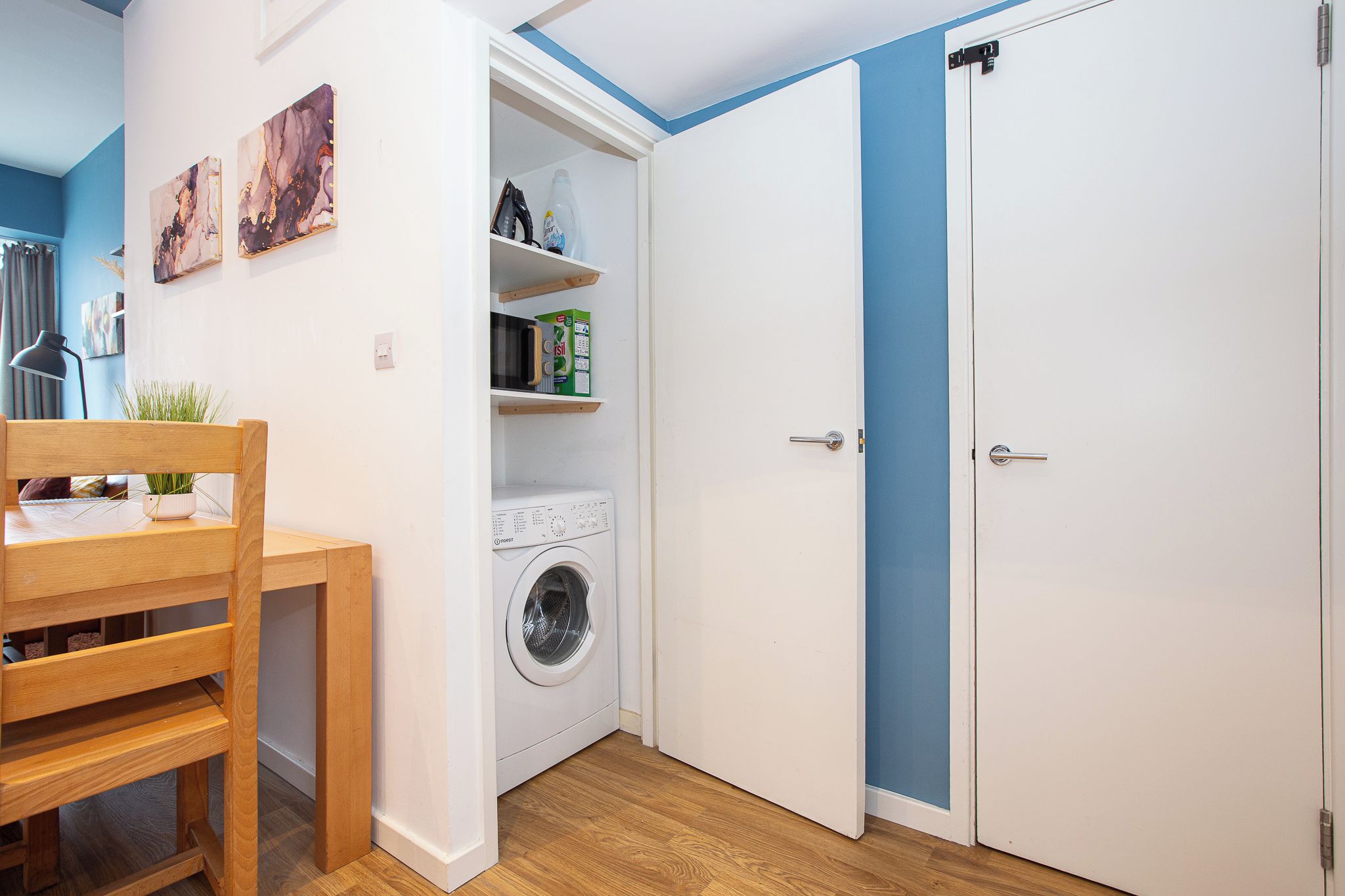 A compact room with a washing machine, a table with chairs, and a wardrobe with a blue accent.