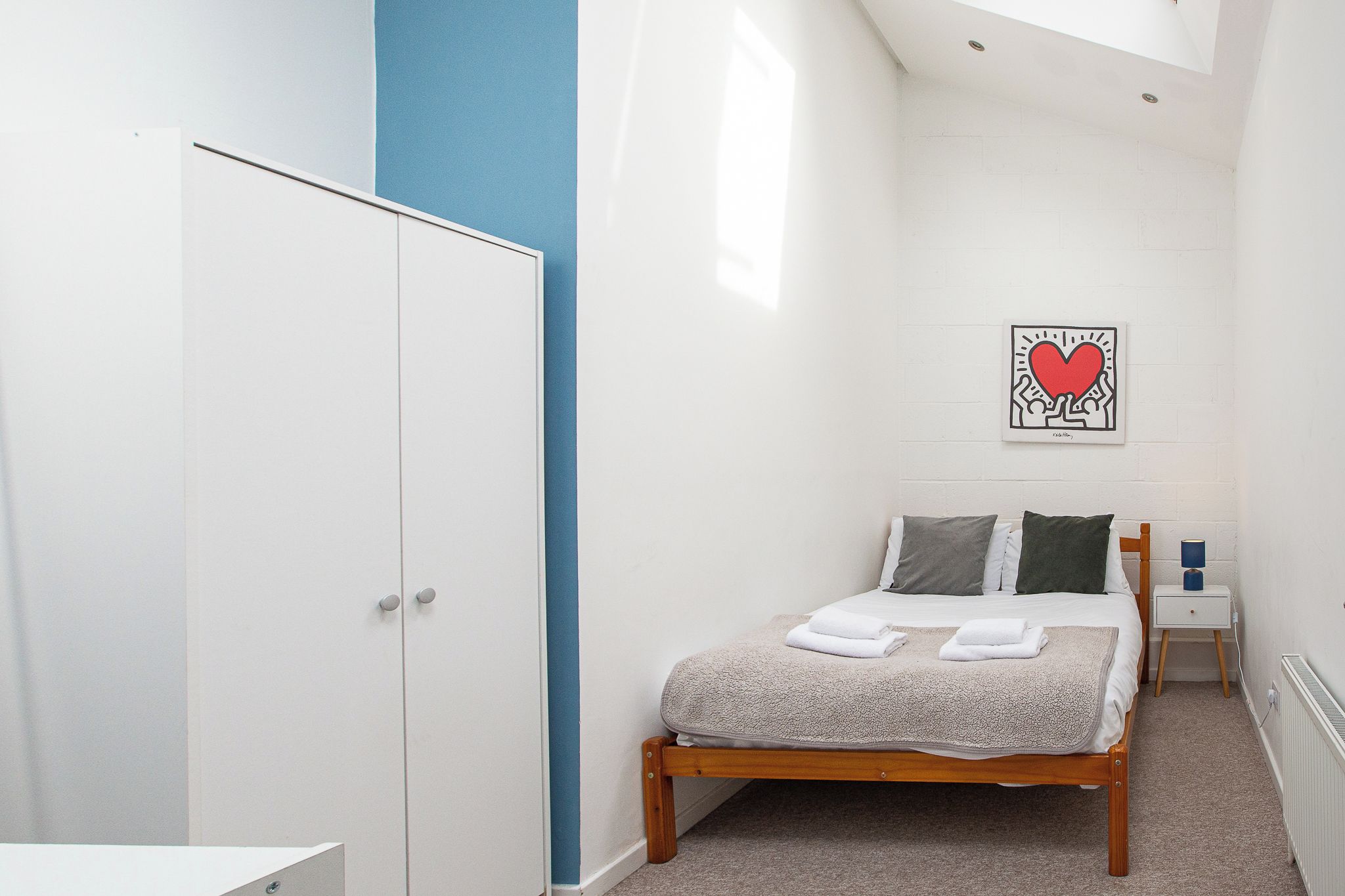 A bedroom with a bed, a wardrobe, a nightstand, and a wall art piece.