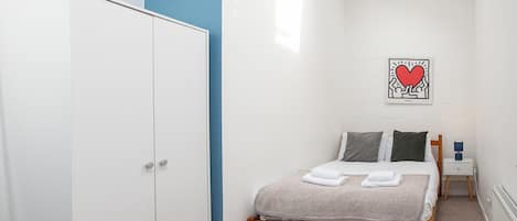 A bedroom with a bed, a wardrobe, a nightstand, and a wall art piece.