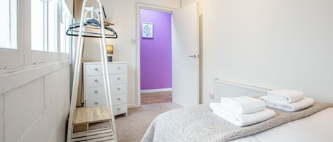 A bedroom with a bed, a ladder, a dresser, and a door leading to another room.