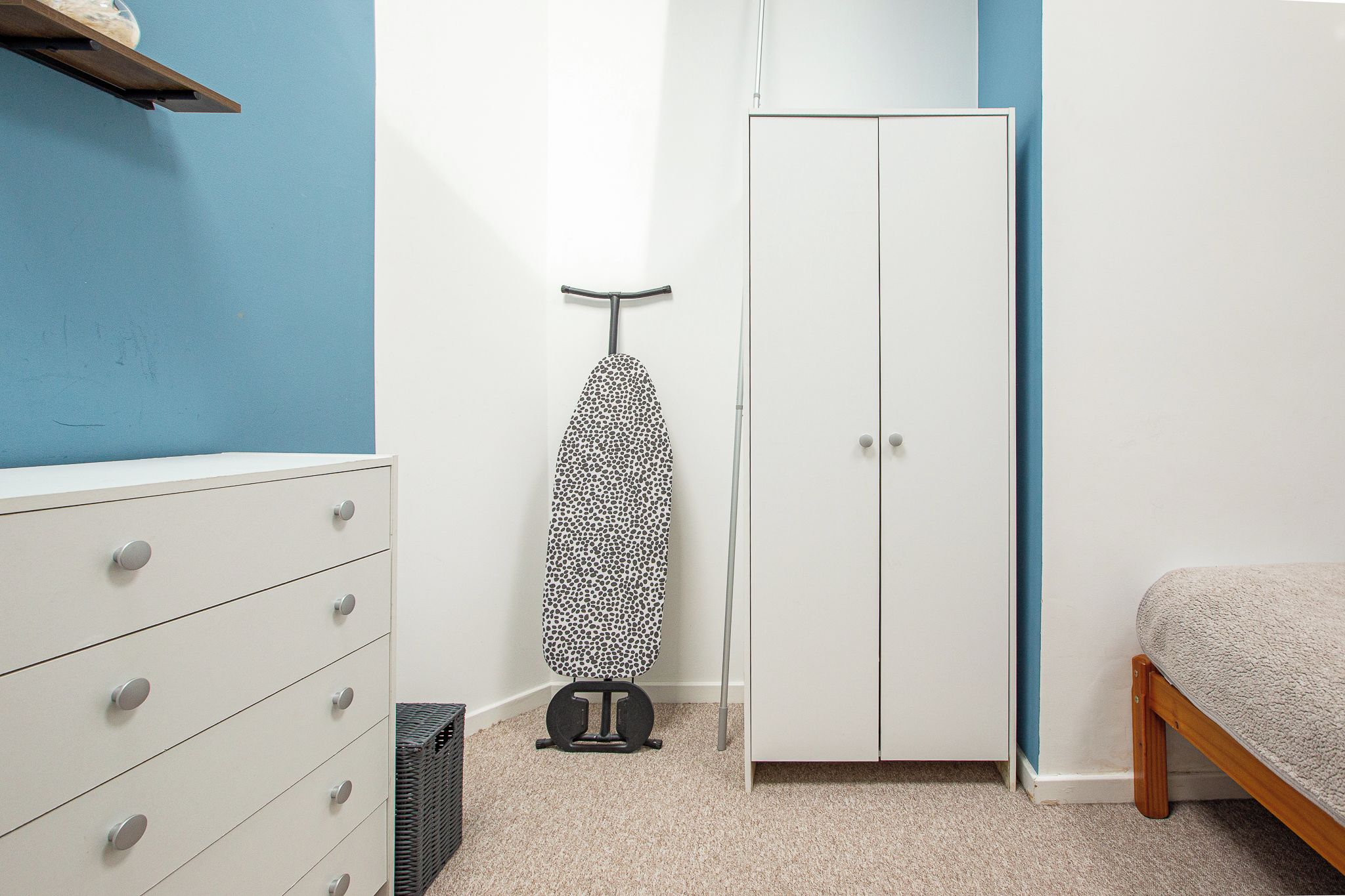 A bedroom with a wardrobe, a bed, a dresser, and an ironing board.