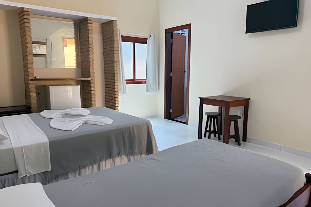 Ein Hotelzimmer mit zwei Betten, einem kleinen Tisch mit Hocker, einem Spiegel und einem an der Wand befestigten Fernseher.