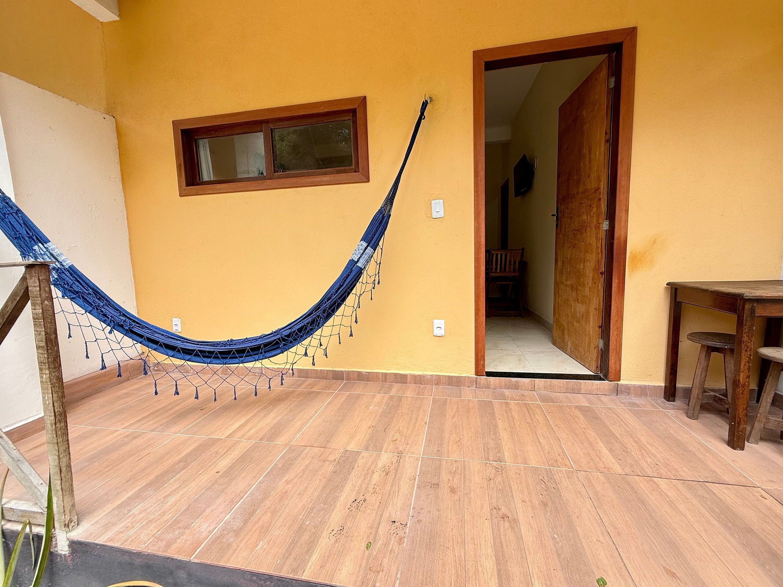 A hammock in a room with wooden flooring, a door leading to another room, and a small table.