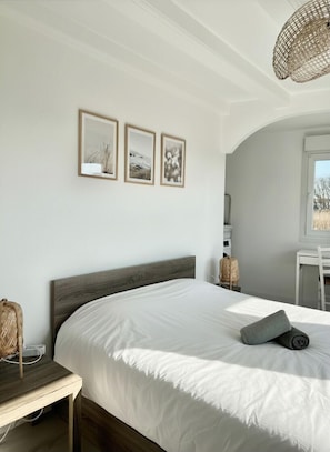 Ein Schlafzimmer mit Bett, Nachttisch, Stuhl und drei gerahmten Bildern an der Wand.