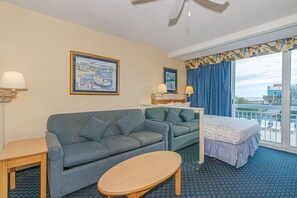 A hotel room with a sofa, a small table, a bed, a balcony with a view, and two wall-mounted lamps. - Yachtsman S202 Studio (Myrtle Beach)