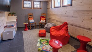 A cozy room with wooden walls, two windows, a flat-screen TV, a red bean bag, and a small table with board games. - Morzine chalet with hot tub. Ski and MTB friendly (Montriond)