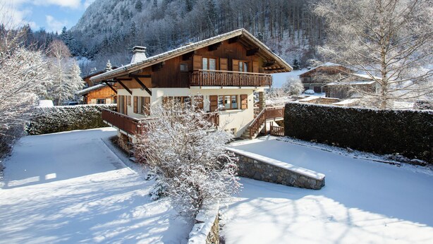 A wooden chalet with a balcony, surrounded by snow-covered trees and a mountain backdrop. - Morzine chalet with hot tub. Ski and MTB friendly (Montriond)