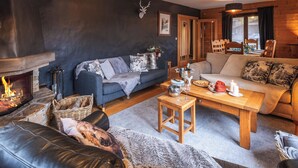 A cozy living room with a fireplace, sofas, a coffee table, and pendant lights. - Morzine chalet with hot tub. Ski and MTB friendly (Montriond)